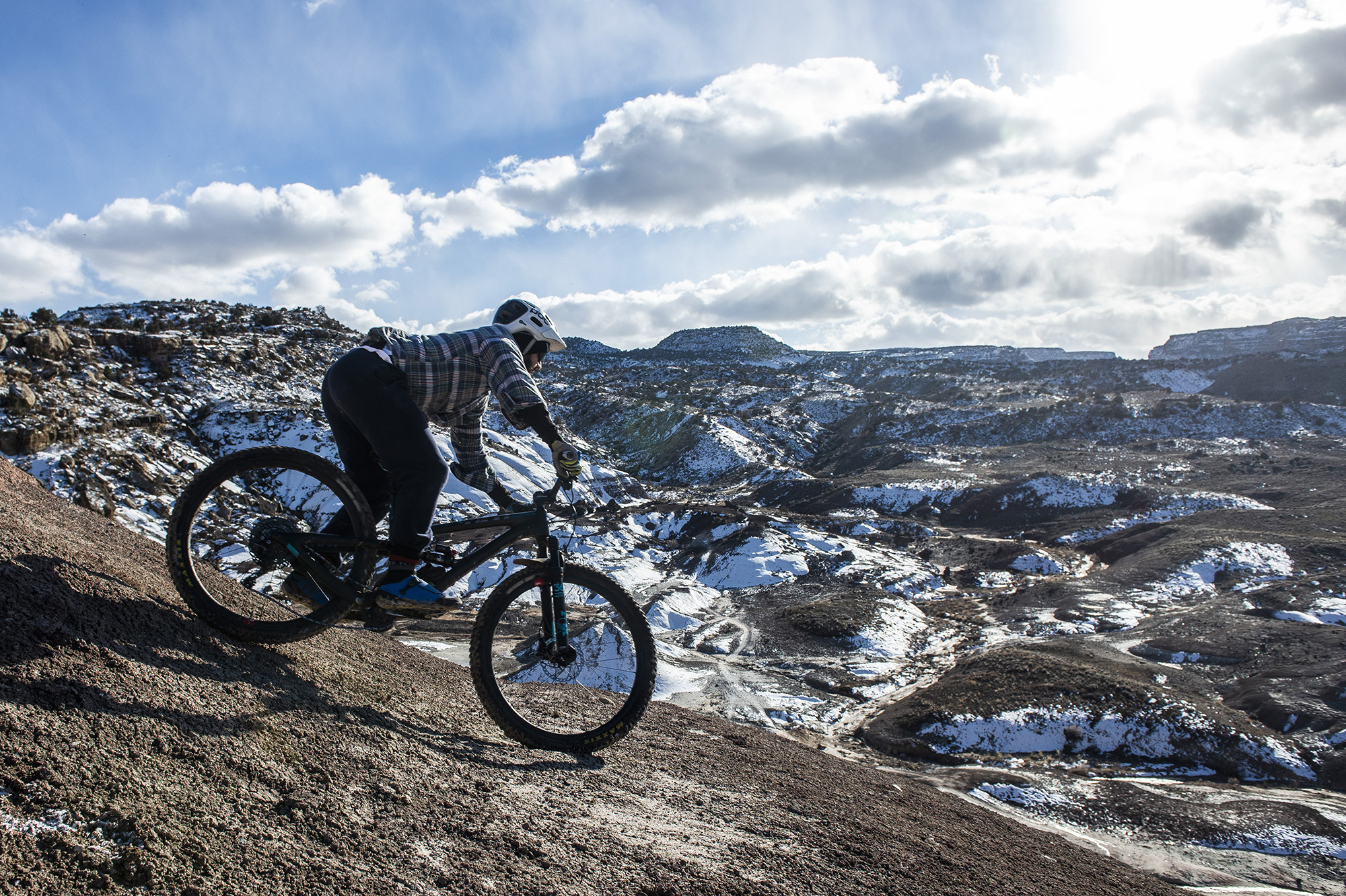 Single mountain biker faces downhill with snow-covered mountain ranges in background