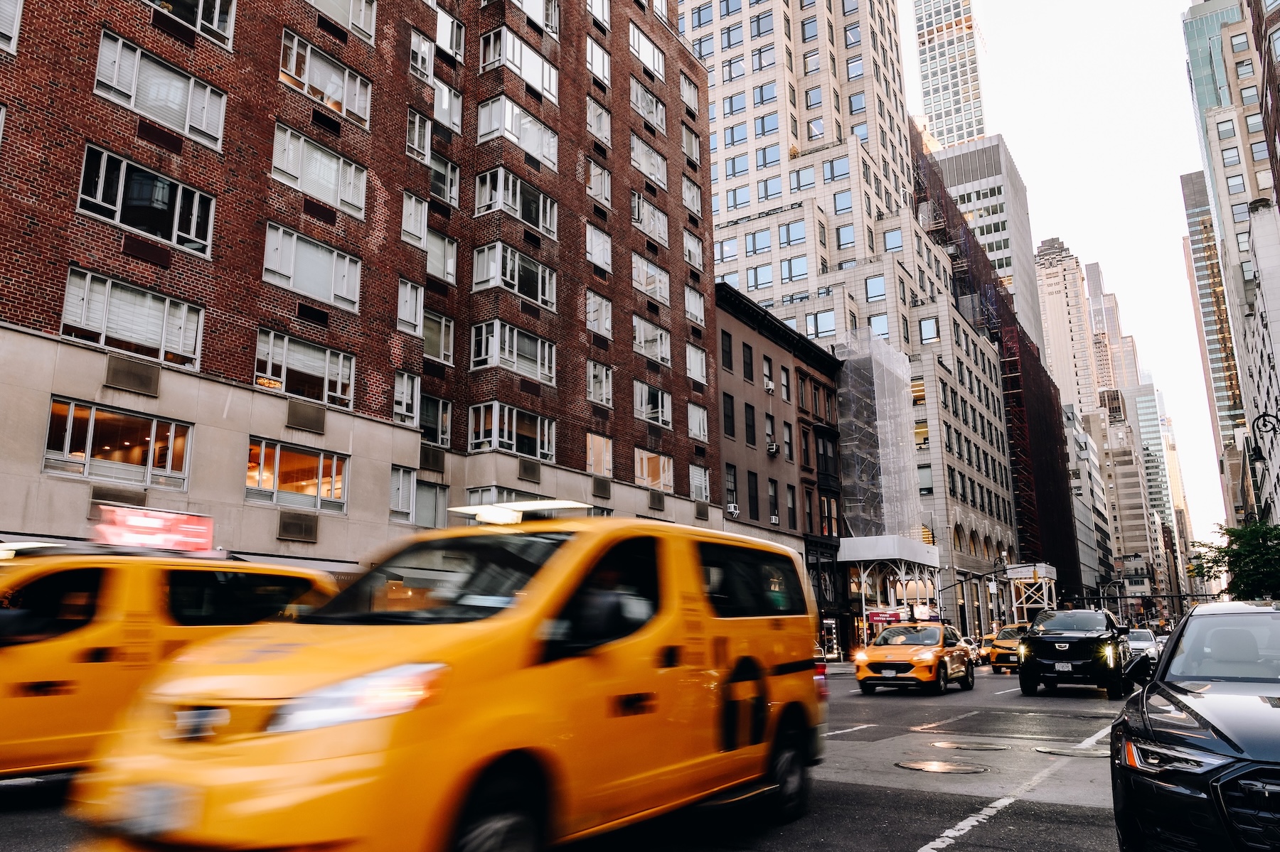 Two yellow New York taxis zooms by, with more traffic in the background.